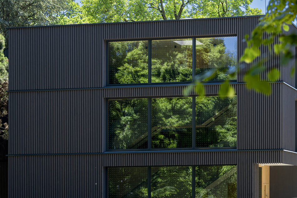 Dark façade of Haus August at Seegut Zeppelin, with large windows framed by trees