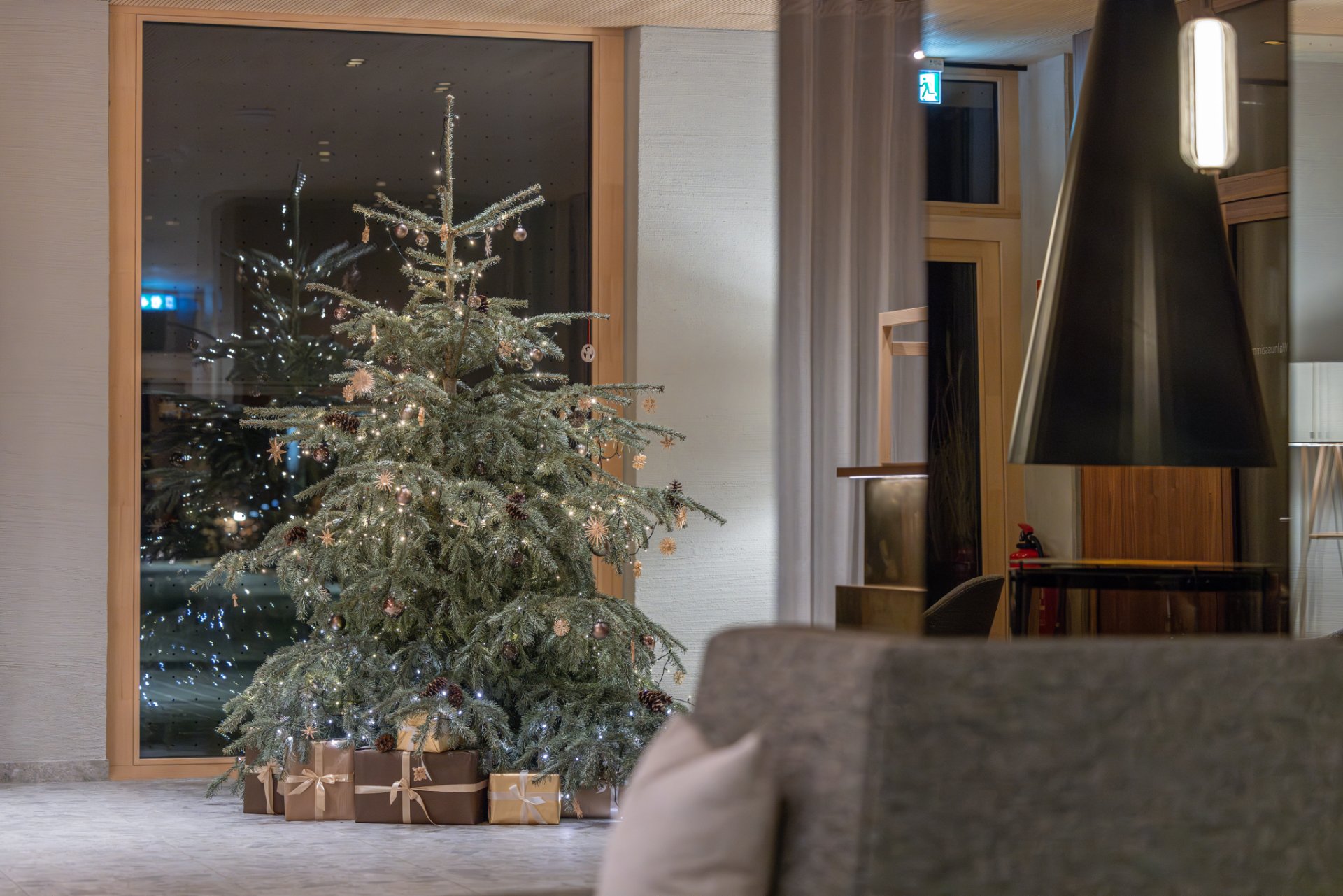 [Translate to English:] Geschmückter Christbaum neben dem Kamin in der Lobby des Seegut Zeppelin am Bodensee am Abend