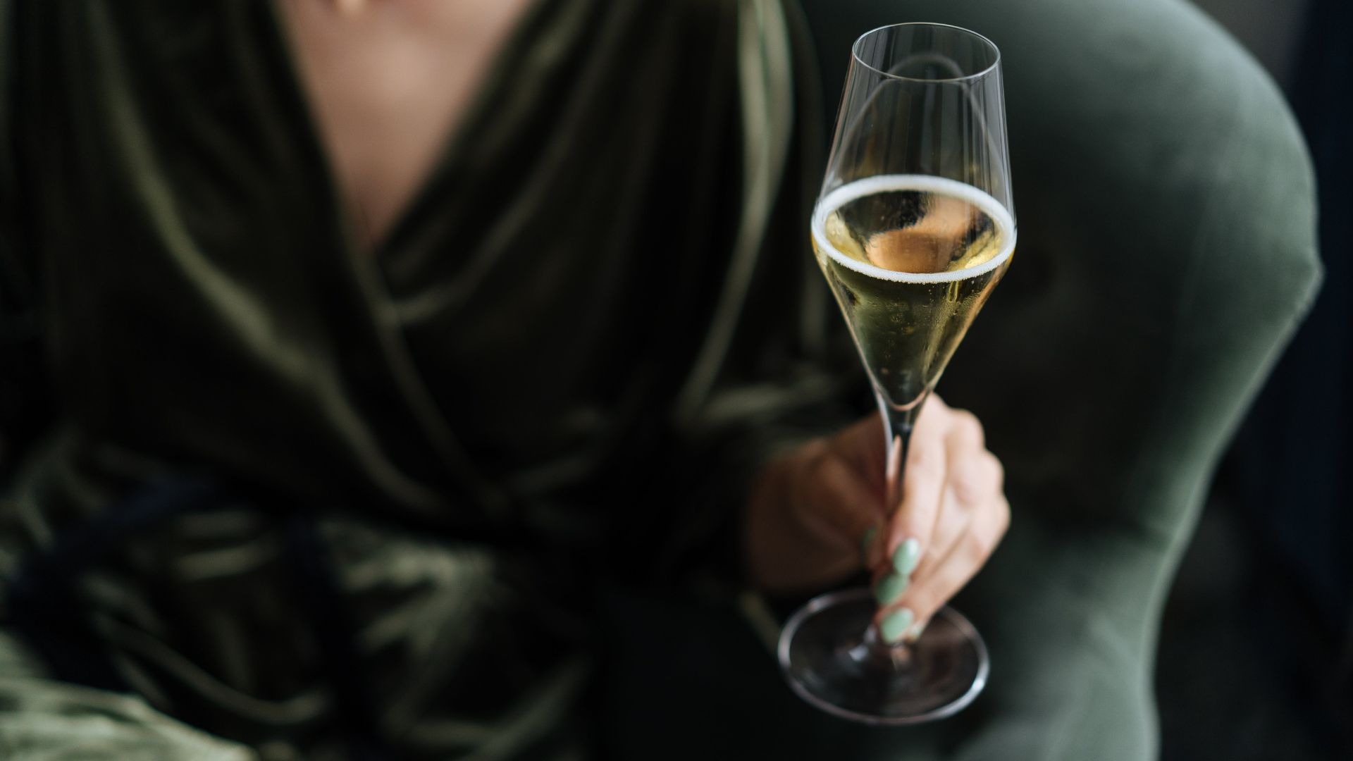 Gast im grünen Samtkleid mit einem Glas Champagner zum Jahreswechsel