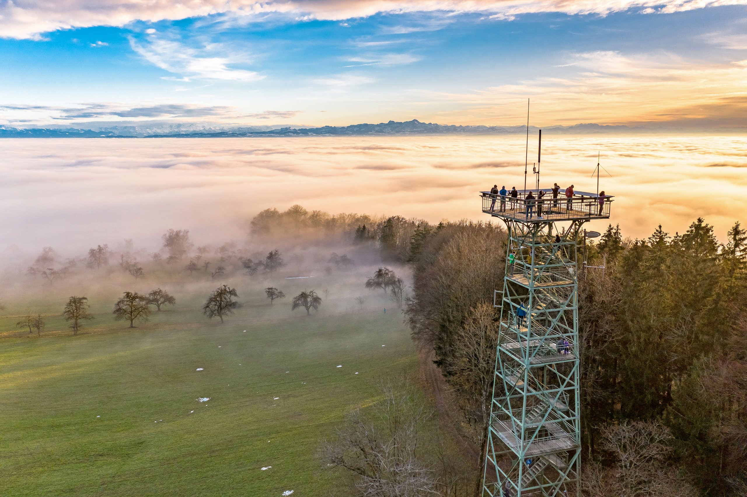 Aussichtsturm über einem Nebelmeer am Bodensee, dahinter die Alpen im Abendlicht