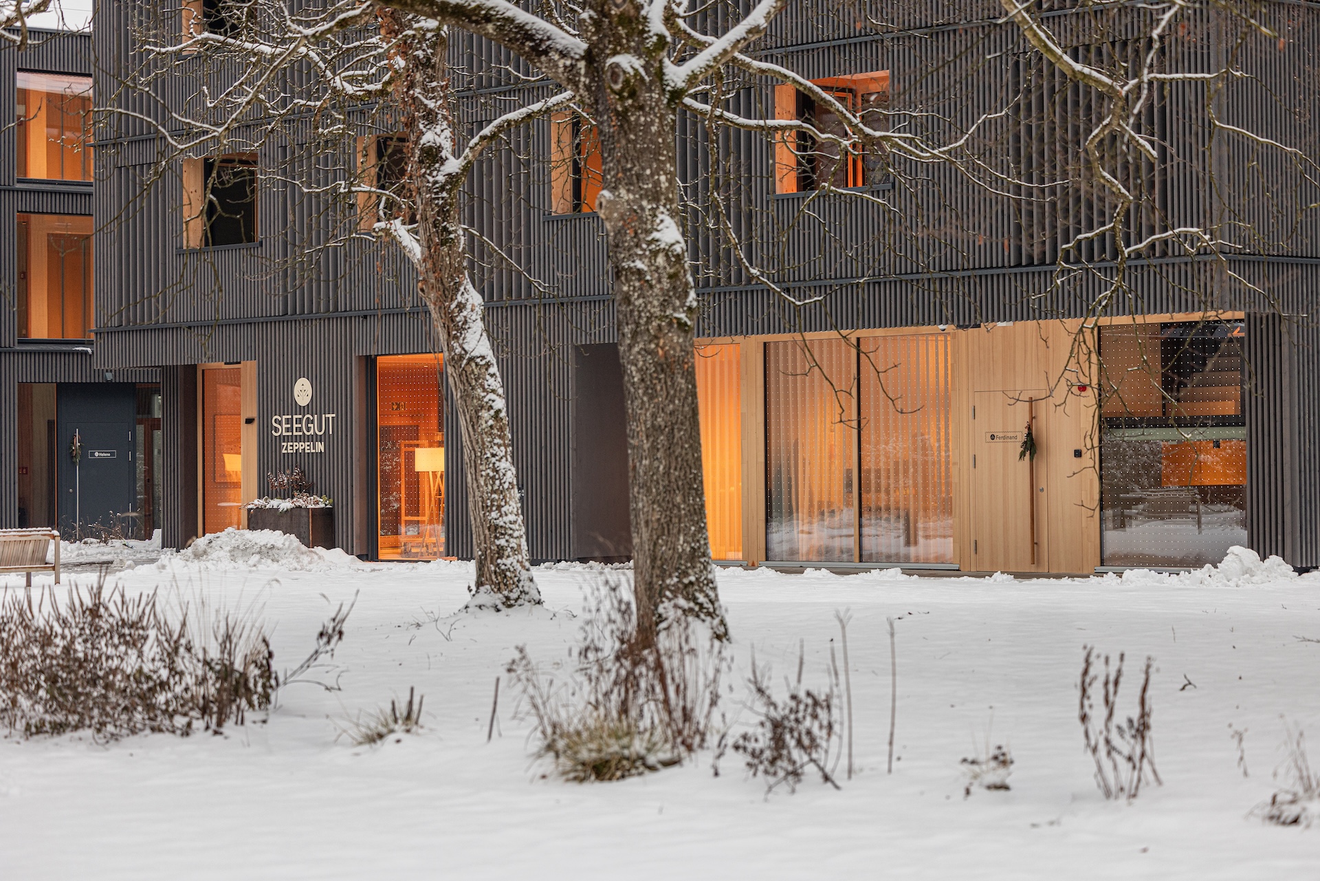 Neubau des Seegut Zeppelin im Schnee mit dunkler Holzfassade und warm beleuchteten Fenstern, Friedrichshafen am Bodensee