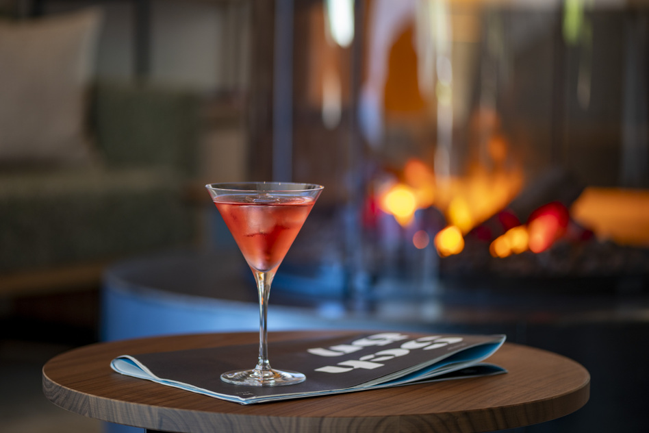 Roter Cocktail im Glas auf einem Holztisch vor dem Kaminfeuer im Seegut Zeppelin am Bodensee