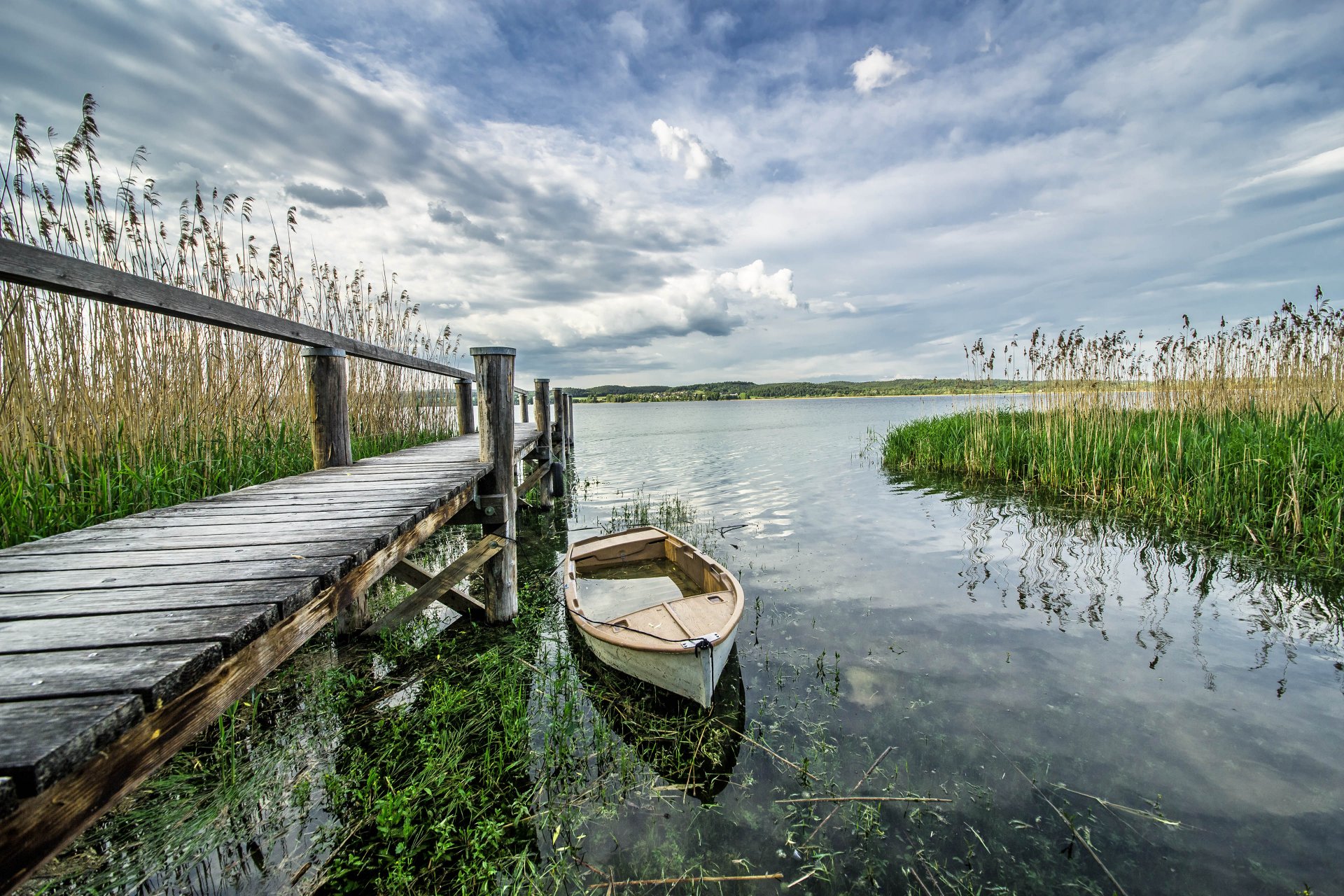 Wooden jetty with a rowing boat in the reeds on Lake Constance under a cloudy sky