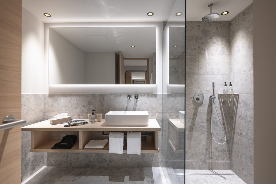 Badezimmer eines Gartenzimmers im Seegut Zeppelin mit Waschtisch, beleuchtetem Spiegel und begehbarer Regendusche