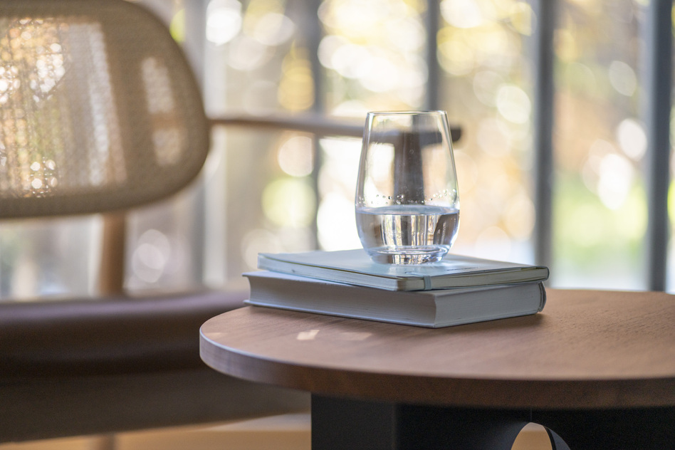 Detail im Haus Ferdinand des Seegut Zeppelin: rundes Holztischchen mit Wasserglas auf Büchern neben einem Rattansessel