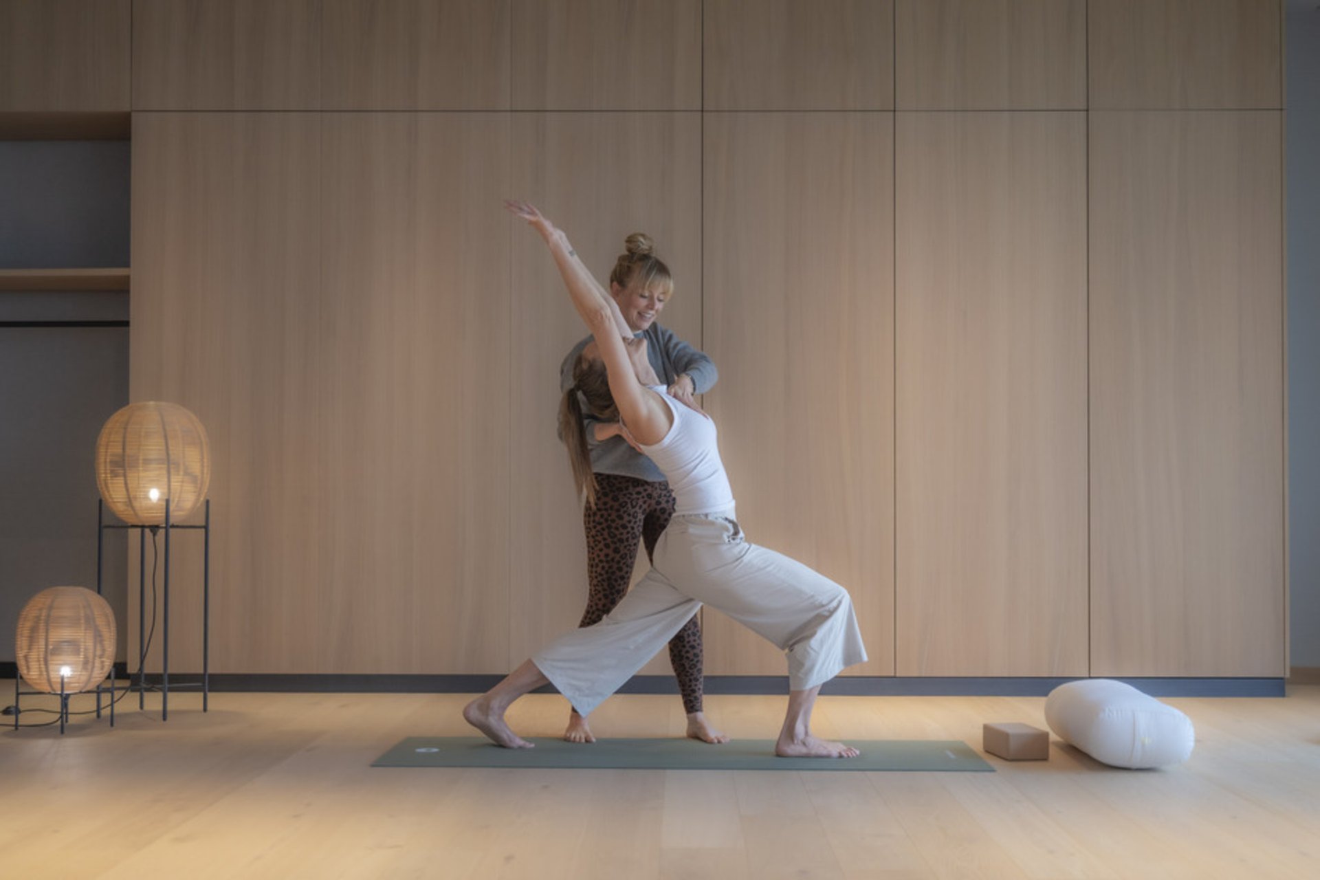 Yogalehrerin Birte begleitet eine Person bei einer Yoga-Übung im holzverkleideten Yogaraum des Seegut Zeppelin